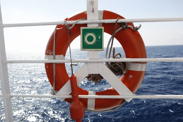 Красный спасательный круг перед синим морем и белым кораблем — стоковое фото