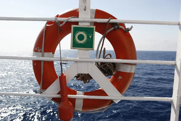 Boa di vita rossa di fronte al mare blu e alla nave bianca — Foto Stock