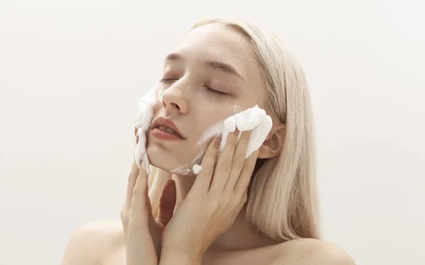 Güzel sarışın hafif bir arka planda yüz köpüğü sürüyor.