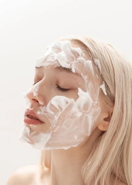 Güzel sarışın hafif bir arka planda yüz köpüğü sürüyor.