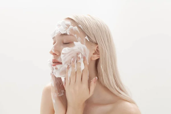 Güzel sarışın hafif bir arka planda yüz köpüğü sürüyor.