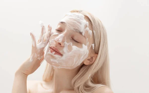 Güzel sarışın hafif bir arka planda yüz köpüğü sürüyor.