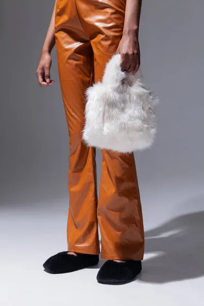 Elinde şık bir kürk çantasıyla deri kahverengi pantolonlu bir kız.