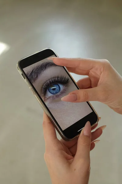 Kız telefonda kirpik uzantılarının fotoğrafına bakıyor.