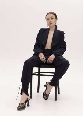 Şık, arsız, takım elbiseli bir kız sandalyede oturuyor.