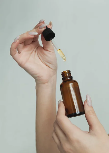 Hafif arka plandaki bir kızın ellerinde bir şişe yüz serumu.