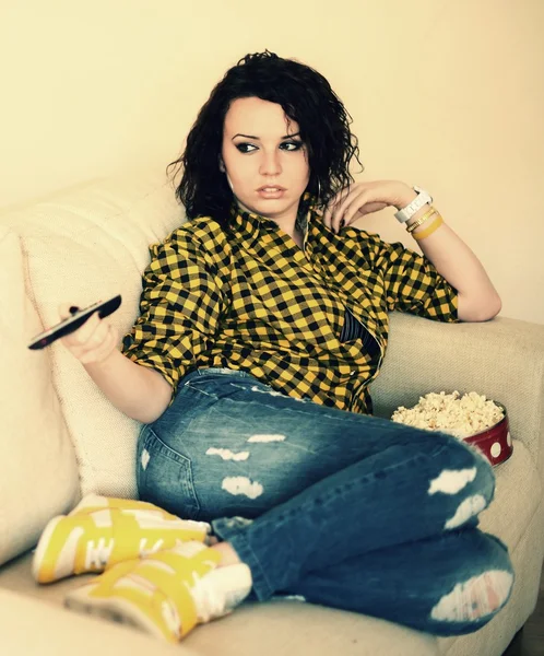 Šťastná mladá žena dívá na televizi na pohovce — Stock fotografie