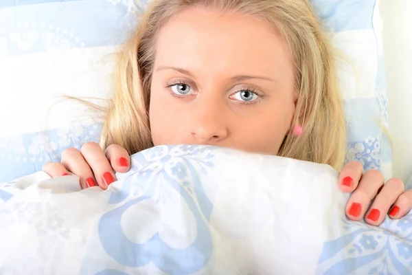 Mujer sonriente bajo un edredón en su dormitorio — Foto de Stock