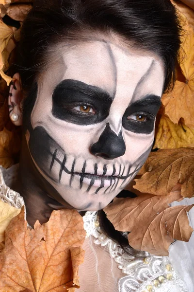 Girl with painting dead mask skull with leaves — Stock Photo, Image