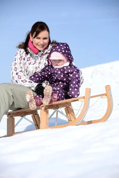 A mãe senta-se no trenó no parque com a criança no inverno — Fotografia de Stock