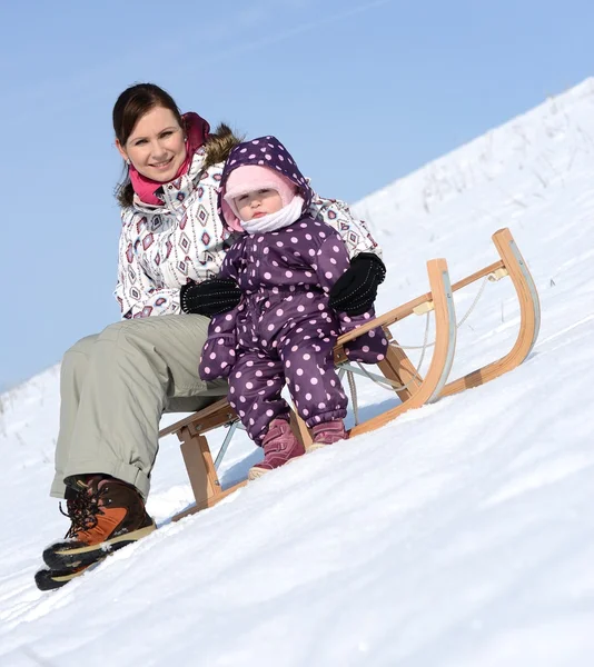 Madre si siede sulla slitta in parco con bambino in inverno — Foto Stock