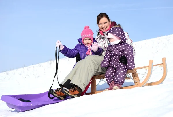 Mother sits on sled in park with children at winter — Stock Photo, Image