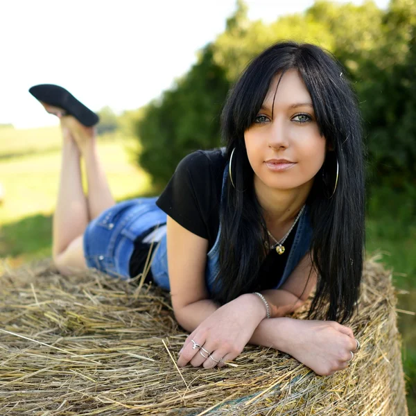 Uma menina em um campo deitado no rolo de feno . — Fotografia de Stock
