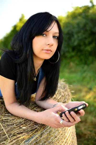 Девушка лежит на сене с мобильным телефоном — стоковое фото