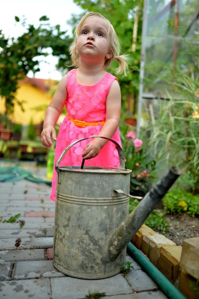 かわいい巻き毛の少女は庭の花に水をまく — ストック写真