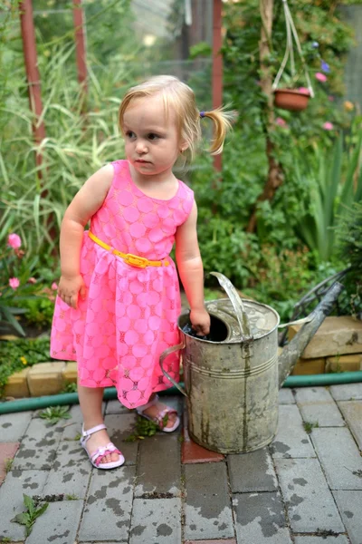 Schattig krullend meisje drenken bloemen in de tuin — Stockfoto