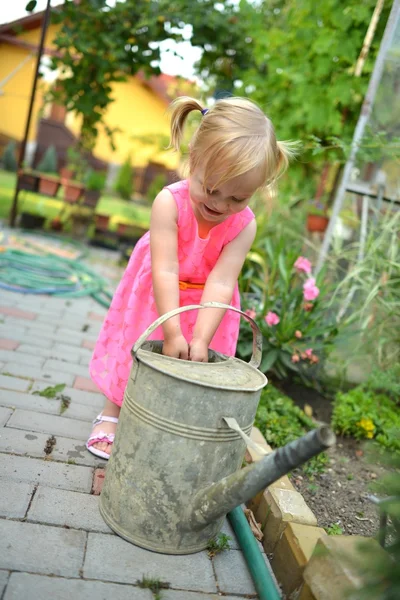 Милая кудрявая девушка поливает цветы в саду — стоковое фото