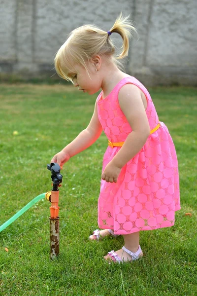 Roztomilá kudrnatá dívka zalévat květiny v zahradě — Stock fotografie