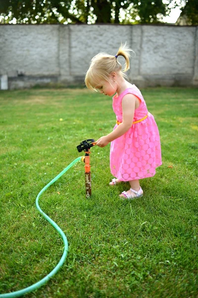 Roztomilá kudrnatá dívka zalévat květiny v zahradě — Stock fotografie