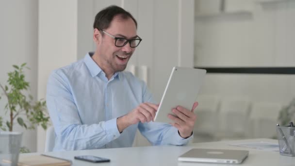 Человек среднего возраста празднует на планшете в офисе — стоковое видео