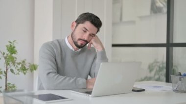 Ofiste dizüstü bilgisayarla otururken uyuklayan yorgun genç adam