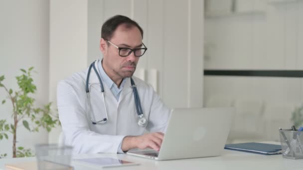 Médico de meia-idade com laptop sorrindo para a câmera no escritório — Vídeo de Stock