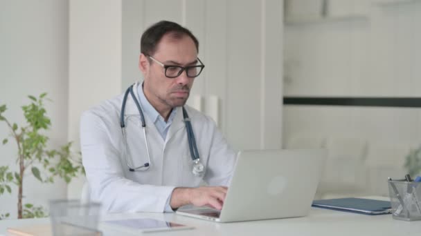Medelålders läkare med bärbar dator Tittar på kameran i Office — Stockvideo