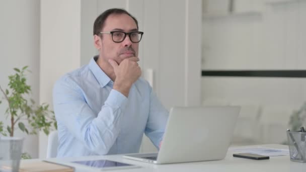 Uomo di mezza età che pensa mentre usa il computer portatile in ufficio — Video Stock