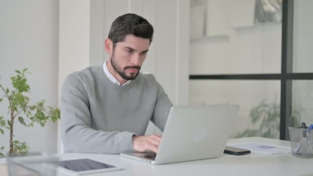 Молодой человек показывает большой палец вниз знак во время использования ноутбука на работе — стоковое видео