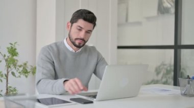 Ofiste dizüstü bilgisayar kullanırken Smartphone ile konuşan genç adam