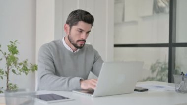 Ofiste dizüstü bilgisayarda çalışan genç adam.