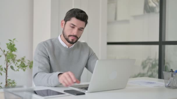 Młody człowiek rozmawia na smartfonie podczas korzystania z laptopa w biurze — Wideo stockowe