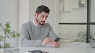 Ofiste akıllı telefon kullanan çekici genç adam. 