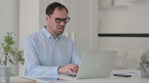 Uomo di mezza età che reagisce alla perdita durante l'utilizzo del computer portatile in ufficio — Video Stock