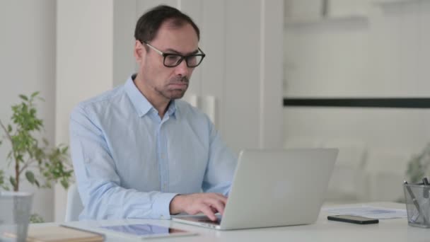 Homem de meia-idade celebrando ao usar o laptop no escritório no banco — Vídeo de Stock