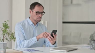 Ofiste akıllı telefon kullanan çekici orta yaşlı adam. 