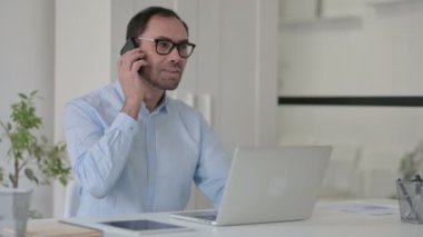 Dizüstü bilgisayar kullanırken Orta yaşlı adam telefonda konuşuyor 