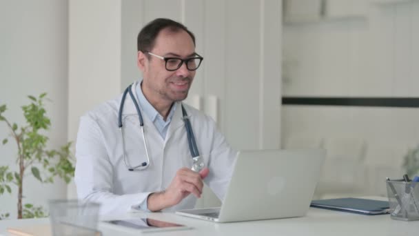 Medelålders läkare talar på videosamtal på laptop i Office — Stockvideo