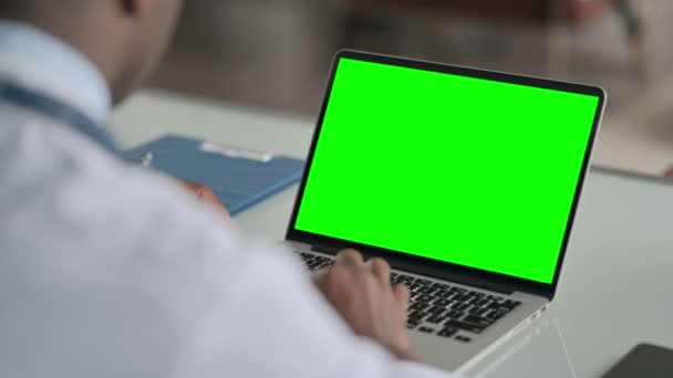 Achteraanzicht van Afrikaanse arts met behulp van laptop met groene chroma scherm — Stockvideo