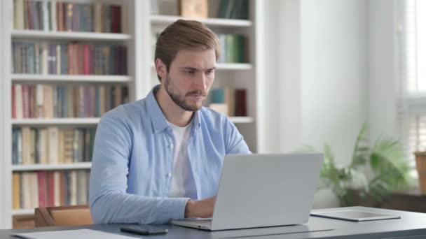Hombre mirando a la cámara mientras usa el ordenador portátil en la oficina — Vídeo de stock