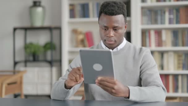 African Man använder surfplatta medan du sitter i biblioteket — Stockvideo