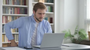 Ofiste dizüstü bilgisayar kullanırken sırt ağrısı çeken adam