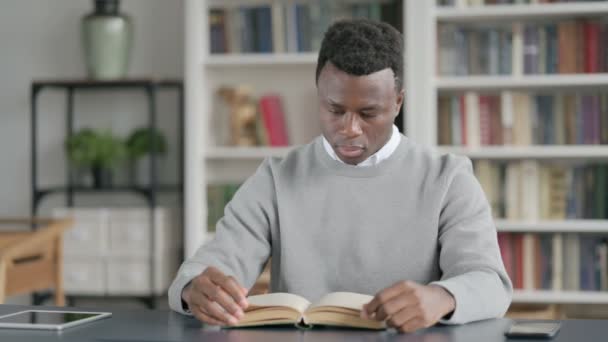 Afrikaanse man die boek leest terwijl hij in de bibliotheek zit — Stockvideo