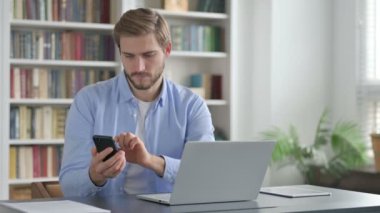 Bilgisayarda çalışırken Smartphone kullanan adam