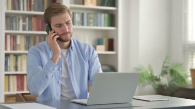 Laptop kullanırken Smartphone 'da Konuşan Adam 