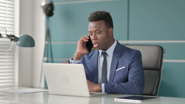 Empresário Africano Falando em Smartphone ao usar Laptop no Office — Vídeo de Stock