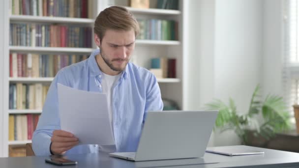 Hombre molesto lectura de documentos mientras se utiliza el ordenador portátil — Vídeo de stock