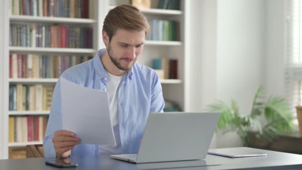 Hombre exitoso leyendo documentos mientras usa el ordenador portátil — Vídeo de stock