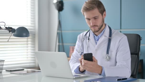 Γιατρός που χρησιμοποιεί Smartphone ενώ εργάζεται σε Laptop στην Κλινική — Αρχείο Βίντεο