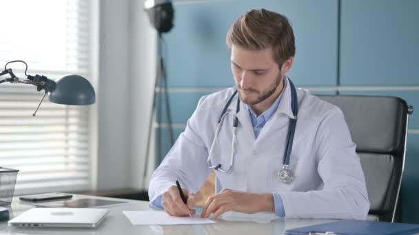 Γιατρός Γράφοντας σε χαρτί, ενώ κάθεται στην κλινική — Αρχείο Βίντεο